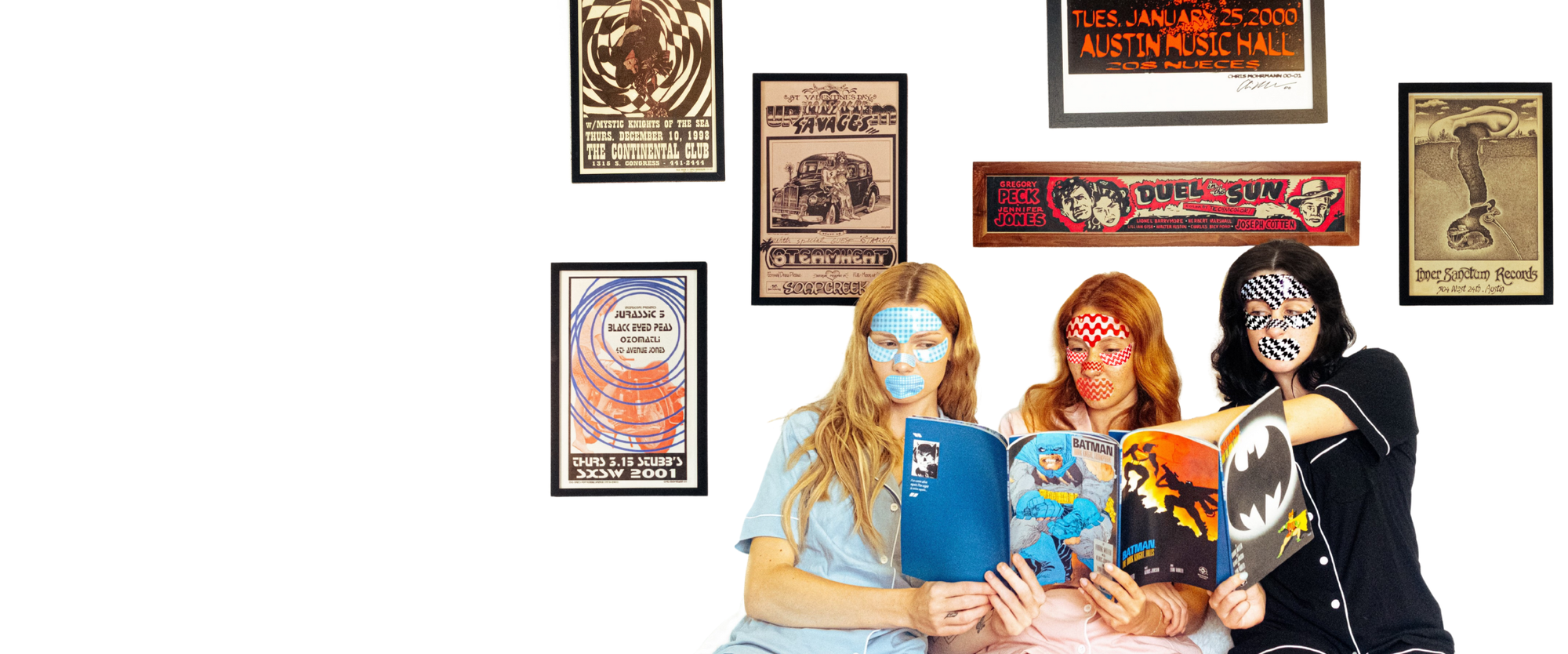 Three friends read comic books while wearing full face masks with posters in the background