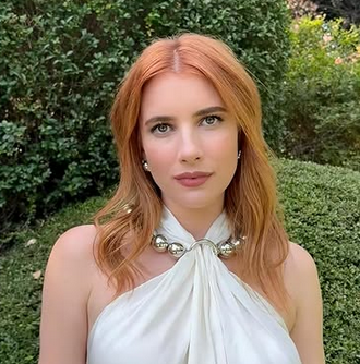 Emma Roberts in a white dress in front of a green background.